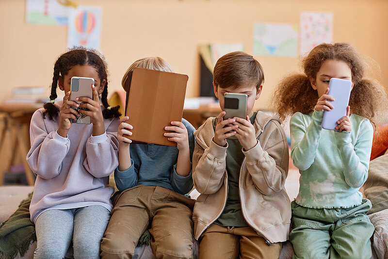 Kinder mit verschiedenen Medientypen (zum Beispiel Handy oder Tablet) in der Hand. 