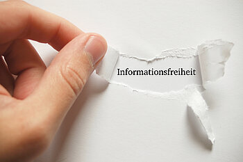 Eine Hand reißt ein Stück Papier ab und legt das Wort Informationsfreiheit frei