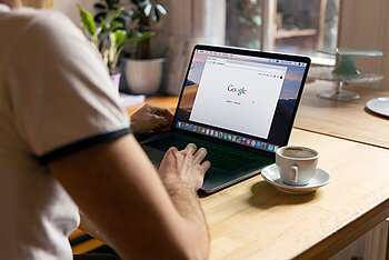 Ein Mann an einem Macbook im Homeoffice, auf seinem Bildschirm ist die Google-Suchmaschine geöffnet
