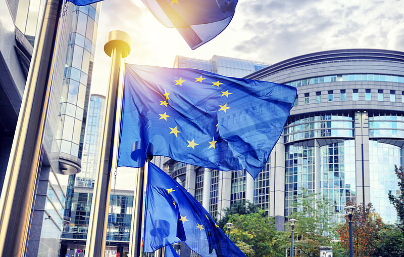 Drei EU-Fahnen wehen vor einer abgerundeten Gebäudefassade