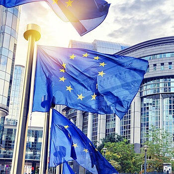 Drei EU-Fahnen wehen vor einer abgerundeten Gebäudefassade